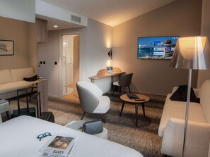 A hotel room with a bed, a desk, a chair, a sofa, a TV, and a lamp. - Mercure Fribourg Centre Remparts (Fribourg)