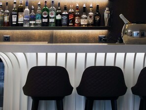 A bar area with various liquor bottles and two upholstered bar stools. - Mercure Fribourg Centre Remparts (Fribourg)