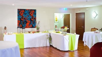 A conference room with tables set for a meeting, a large abstract painting on the wall, and a door with a light above it.