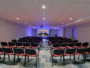 A conference room with rows of chairs, a projector screen, and a presentation area. - Mercure Fribourg Centre Remparts (Fribourg)