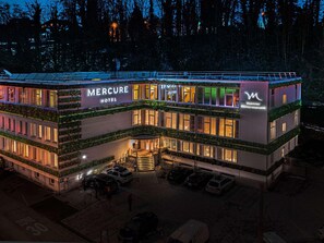 A multi-story hotel with a prominent 'Mercure Hotel' sign, a parking area, and a building with a green facade. - Mercure Fribourg Centre Remparts (Fribourg)