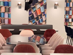 A modern lounge area with a glass table, cushioned chairs, and walls decorated with spools of thread. - Mercure Fribourg Centre Remparts (Fribourg)