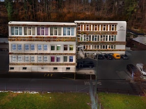 A multi-story building with a white facade, multiple windows, and a parking area with cars. - Mercure Fribourg Centre Remparts (Fribourg)