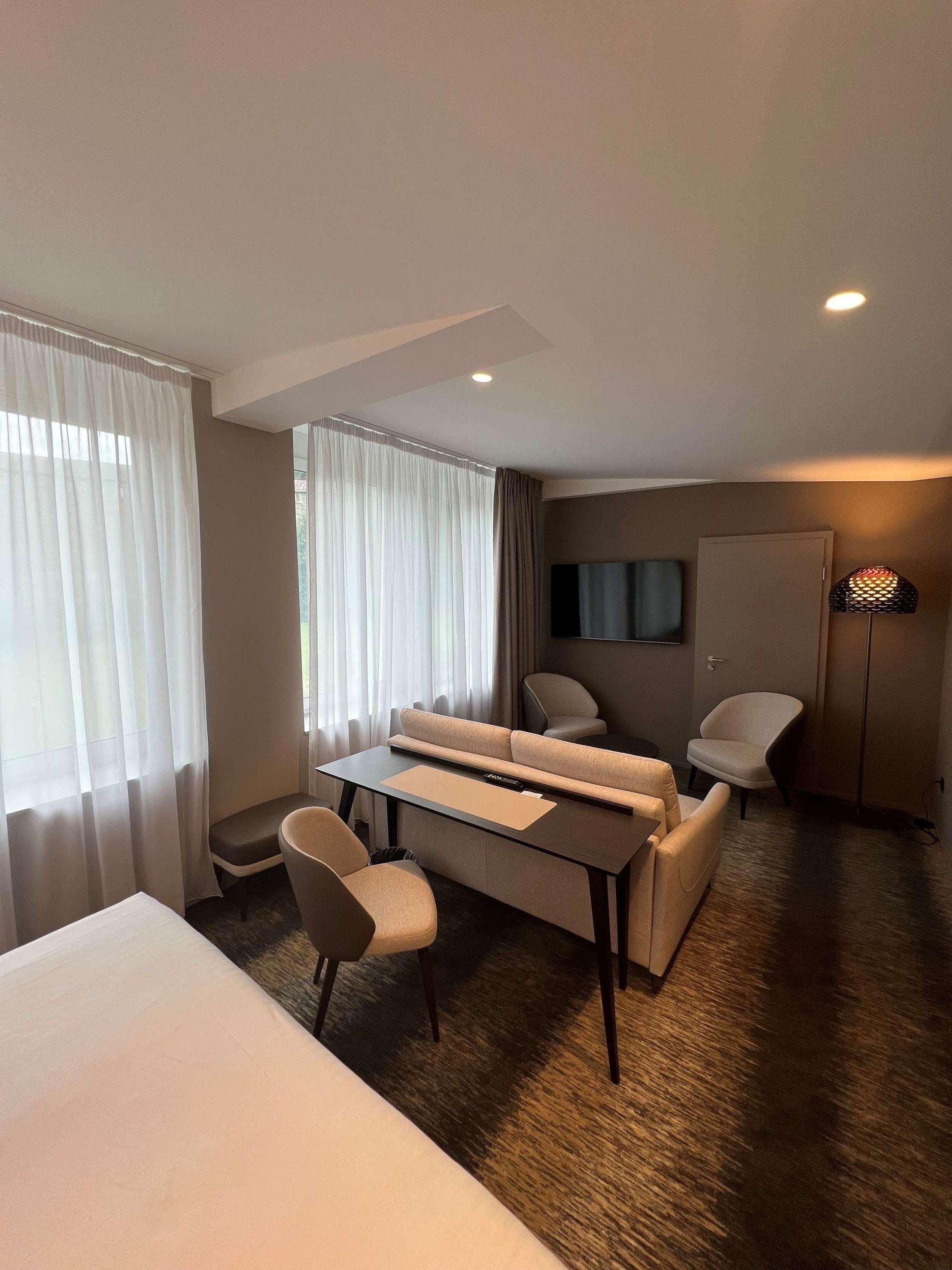 Une chambre d’hôtel avec un lit, un canapé, une petite table, une chaise, une télévision et une lampe.