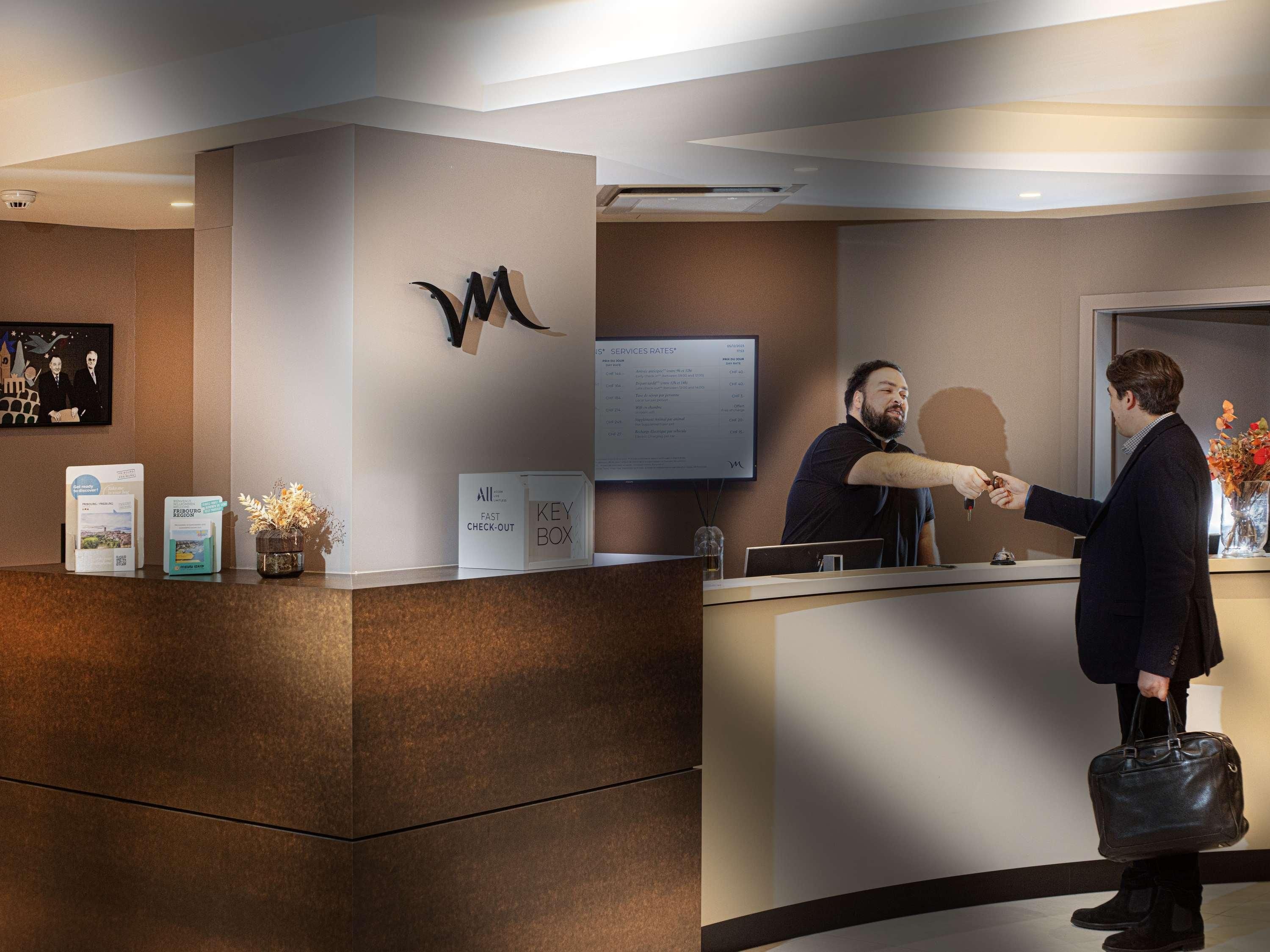 A reception desk with a modern design, a mounted logo, a digital screen displaying rates, and a key box.