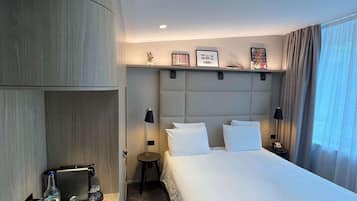A hotel room with a bed, bedside tables, a desk with a coffee machine, and a wall-mounted shelf.