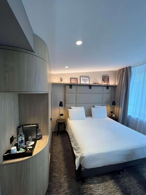 Habitación de hotel con cama, mesitas de noche, escritorio con cafetera y estante en la pared.