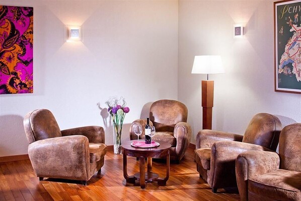 A room with four leather armchairs, a wooden coffee table with a bottle and glasses, a vase with flowers, and a lamp. - Mercure Fribourg Centre Remparts (Fribourg)