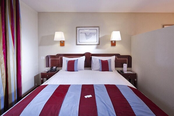A hotel room with a large bed, two bedside tables with lamps, a telephone, and a framed picture on the wall. - Mercure Fribourg Centre Remparts (Fribourg)