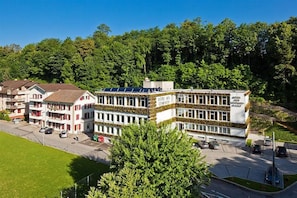 A multi-story hotel with a central atrium, surrounded by greenery and other buildings. - Mercure Fribourg Centre Remparts (Fribourg)