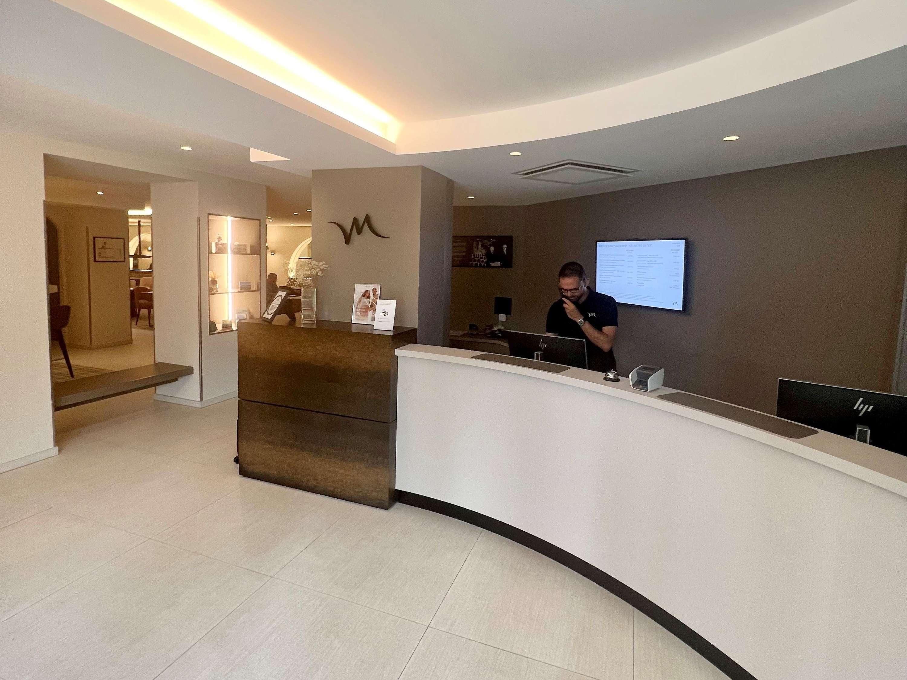 A reception desk with a computer, a framed picture, and a wall-mounted screen.