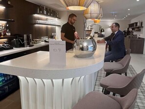 Zona bar moderna con bancone, un'originale composizione centrale in metallo e posti a sedere per gli ospiti.