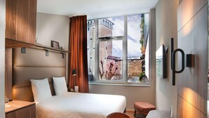 A modern hotel room with a bed, desk, laptop, and a view of a cityscape. - Mercure Fribourg Centre Remparts (Fribourg)