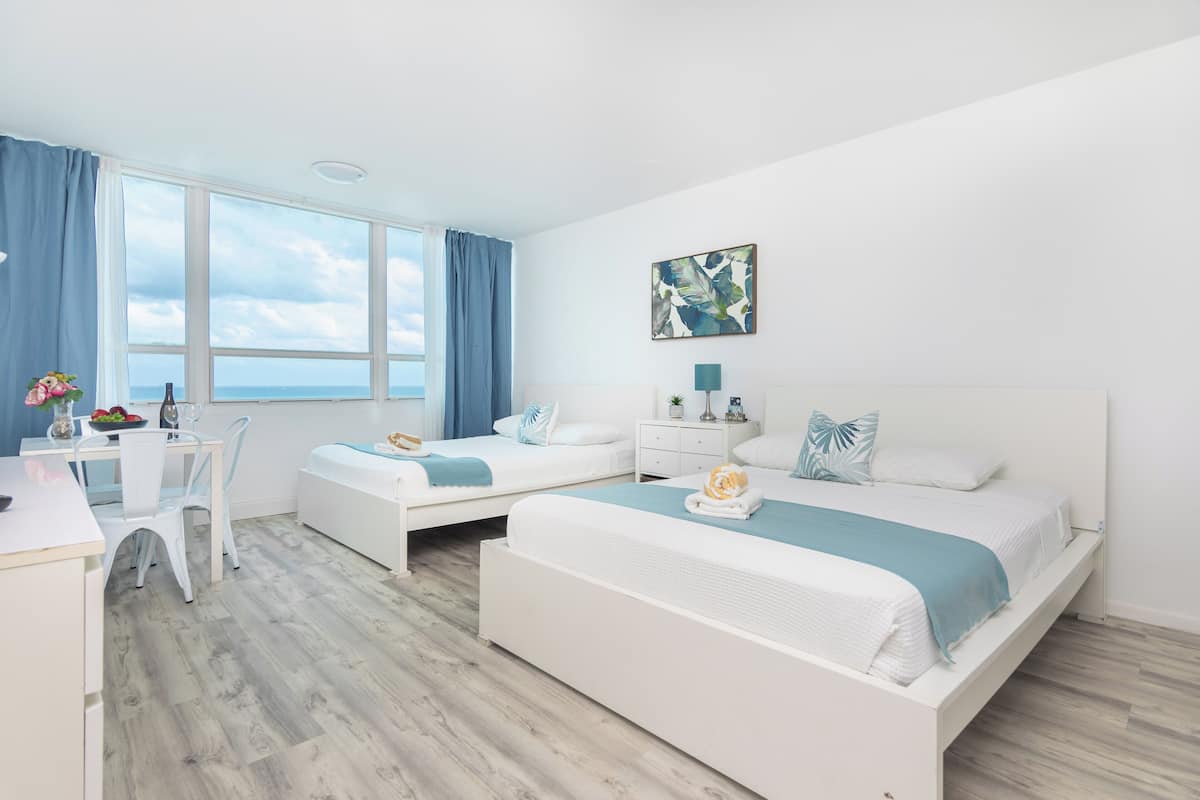 A hotel room with two beds, a desk, and a view of the sea.