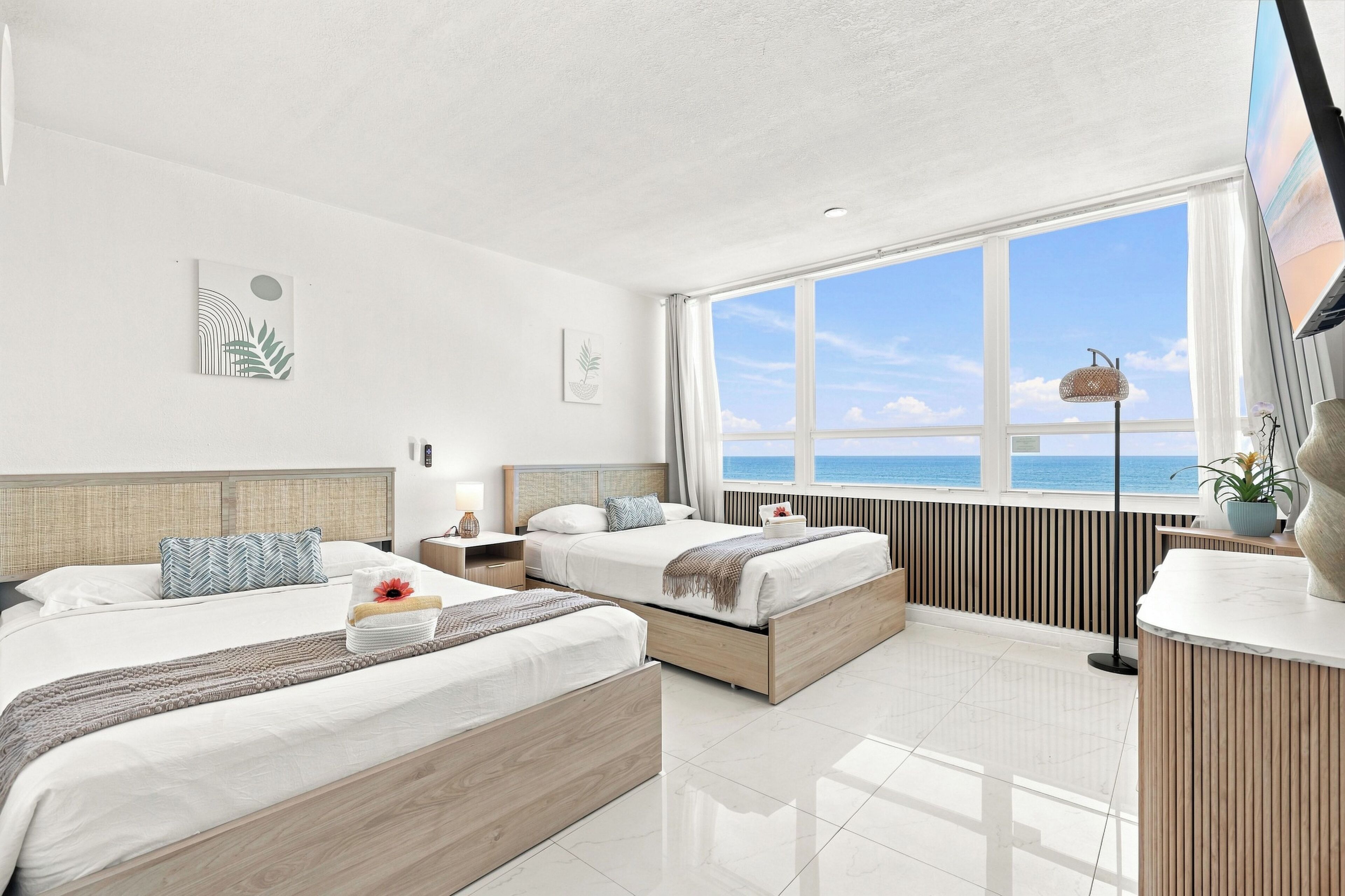 Une chambre d’hôtel avec deux lits, une grande fenêtre donnant sur la mer et un design moderne.