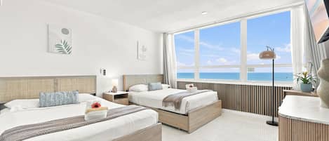 A hotel room with two beds, a large window with a view of the sea, and a modern design.
