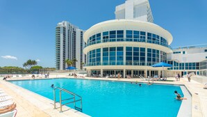 A pool area with a large circular building, a tall adjacent building, and a clear sky. - Girasole Suites (Miami Beach)