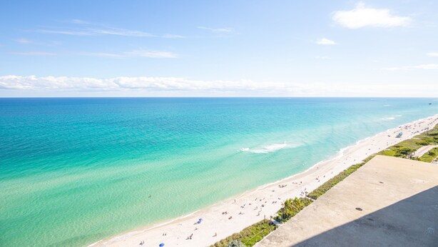 Une plage à l’eau turquoise et limpide, avec un rivage sablonneux et une plateforme d’observation en béton.