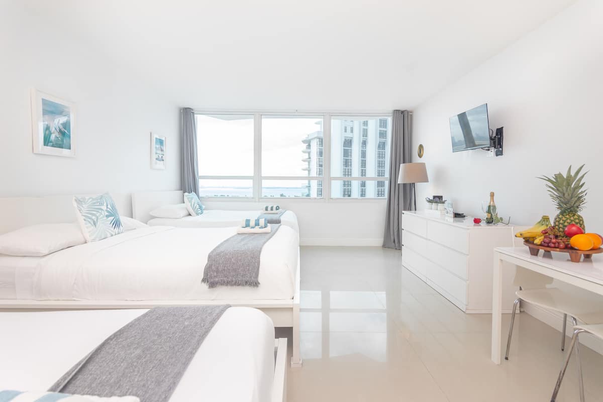A modern hotel room with a large bed, a desk, and a view of the cityscape.