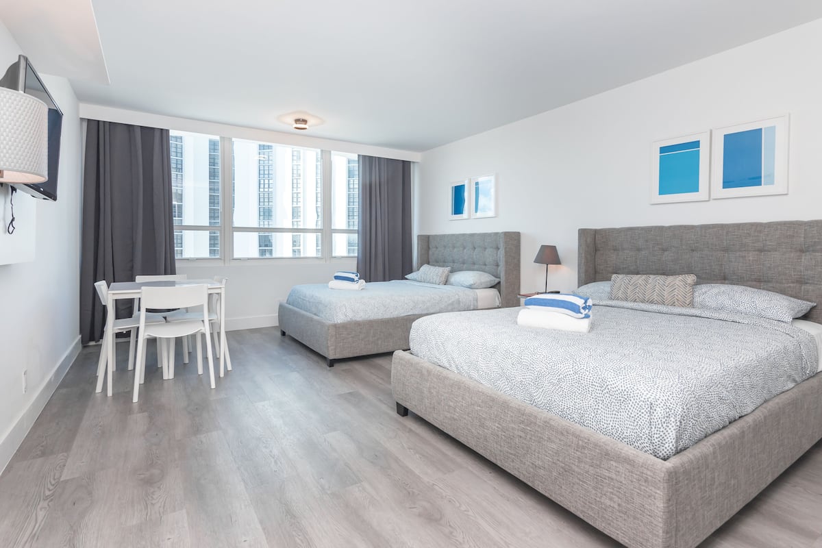 A modern hotel room with two beds, a desk, and a chair.