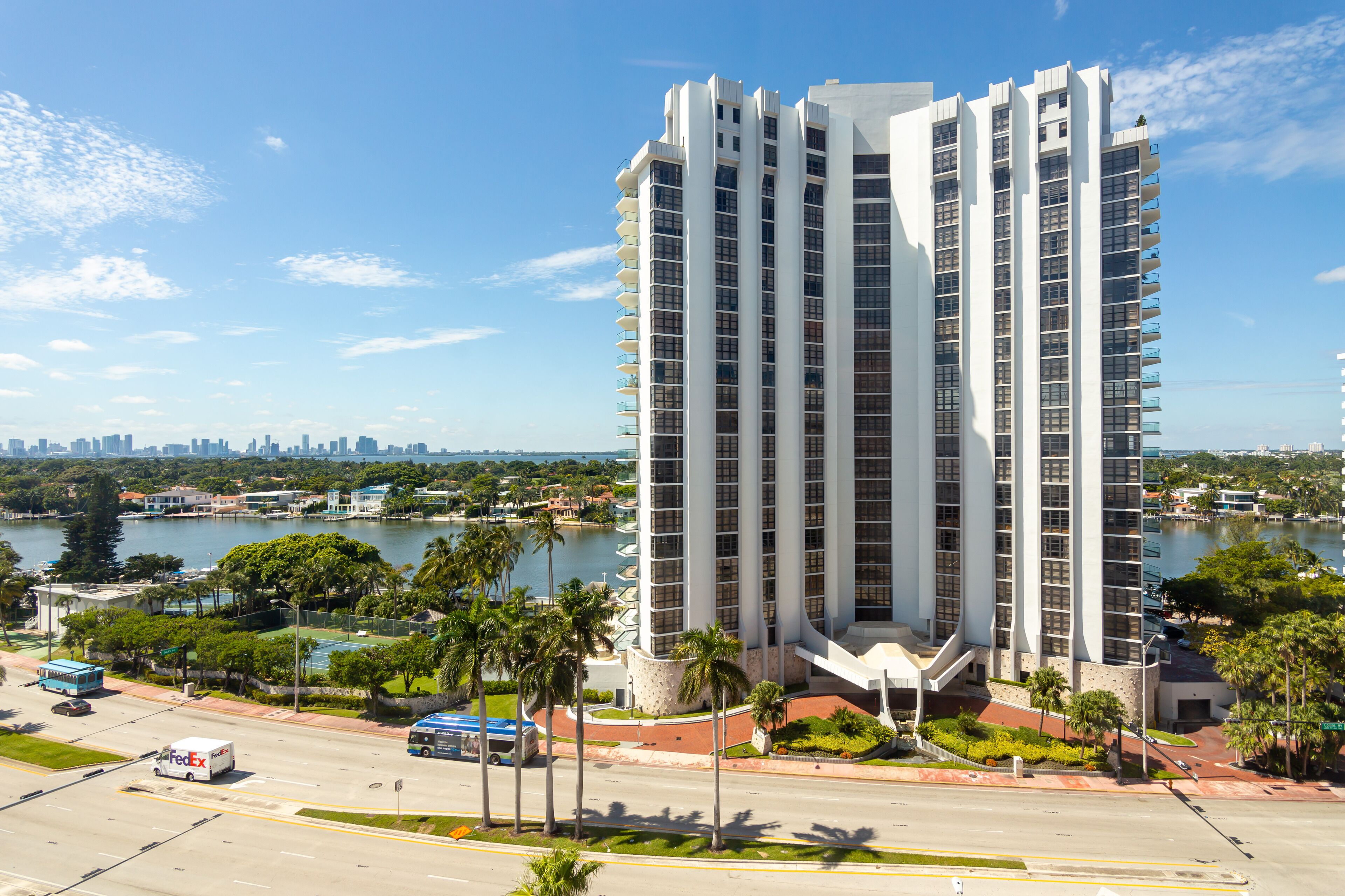A high-rise hotel with a modern design, located near a body of water with a city skyline in the background.