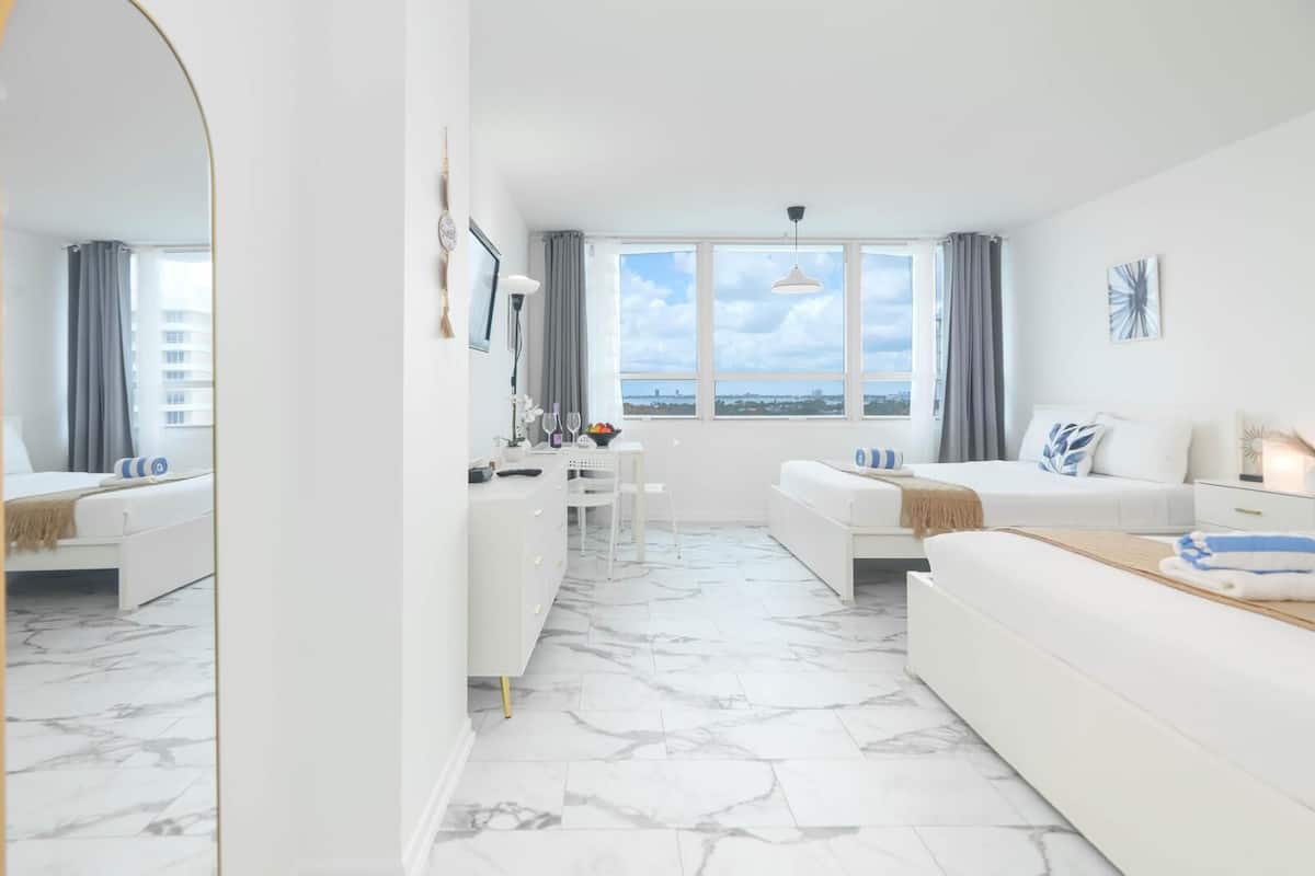 A modern hotel room with a large bed, a sofa, a desk, and a view of the city.