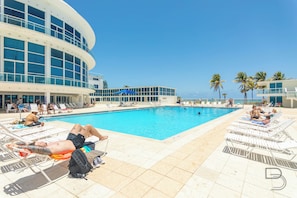 A pool area with lounge chairs and a building with large windows.