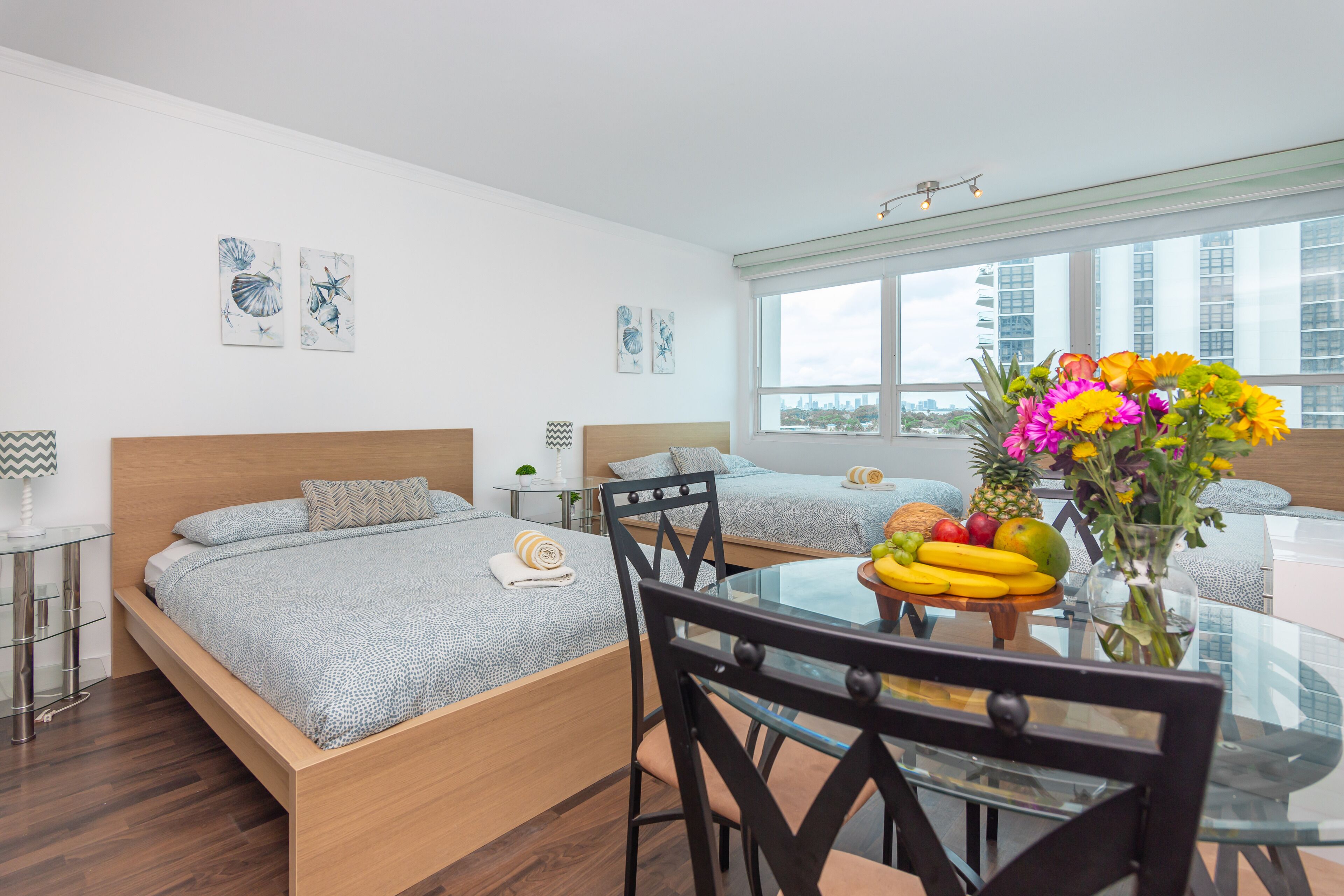 Habitación de hotel moderna con una cama grande, una mesa de comedor con fruta y vistas a la ciudad.