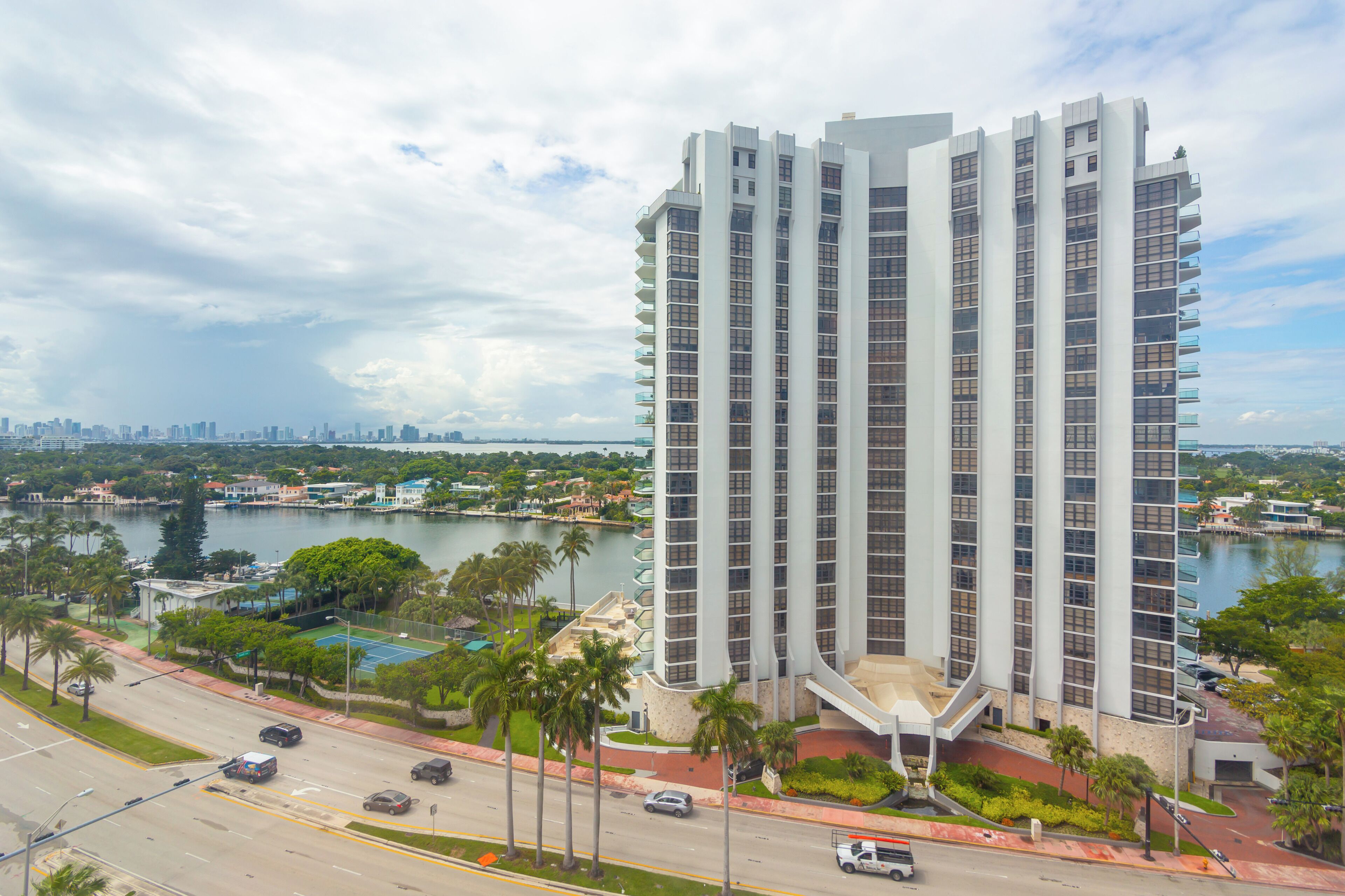 A high-rise building with a modern architectural design, situated near a body of water with a city skyline in the background.