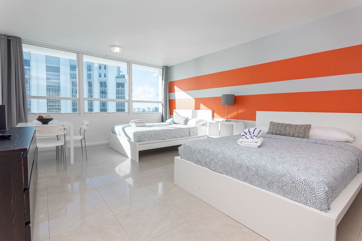 A modern hotel room with a large bed, a desk, and a view of the cityscape.