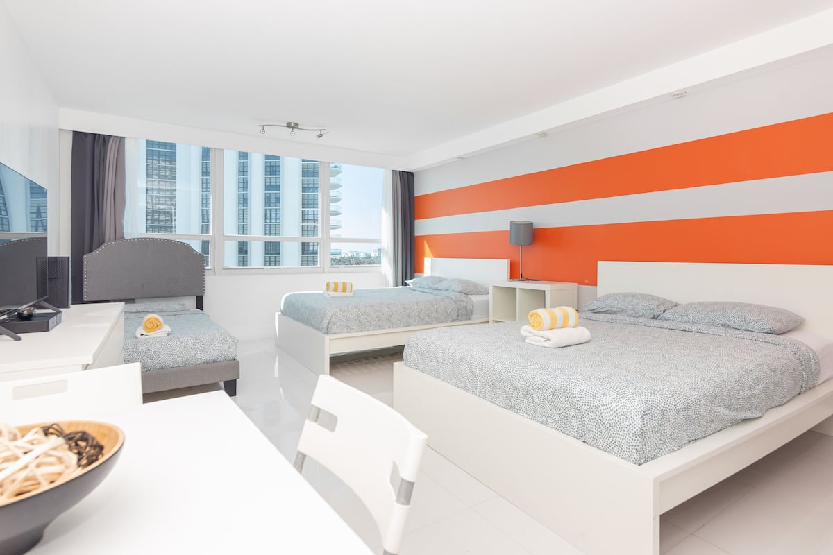 A modern hotel room with two beds, a desk, and a view of tall buildings.