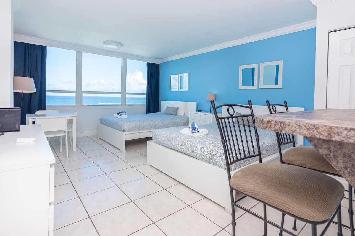 A hotel room with a bed, a desk, a chair, and a view of the sea.