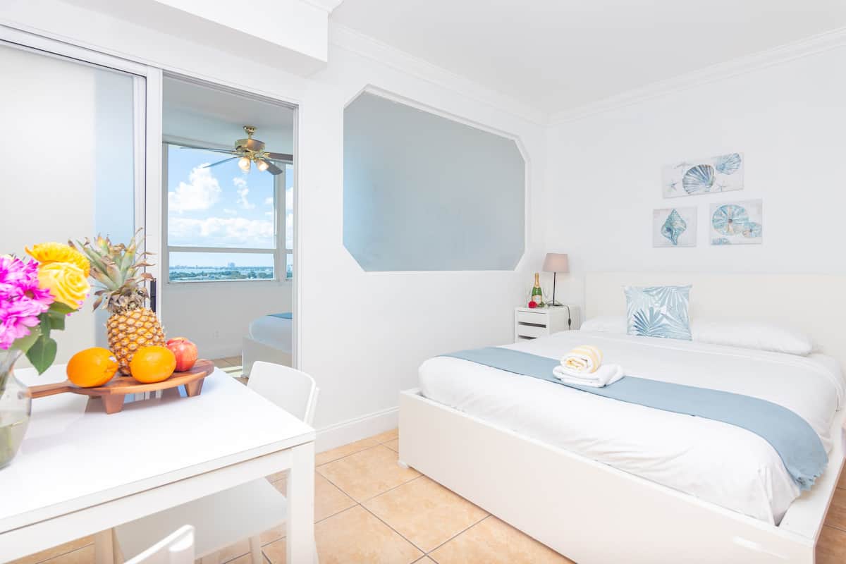 A modern bedroom with a bed, a bedside table, a window with a view, and a fruit basket on a table.