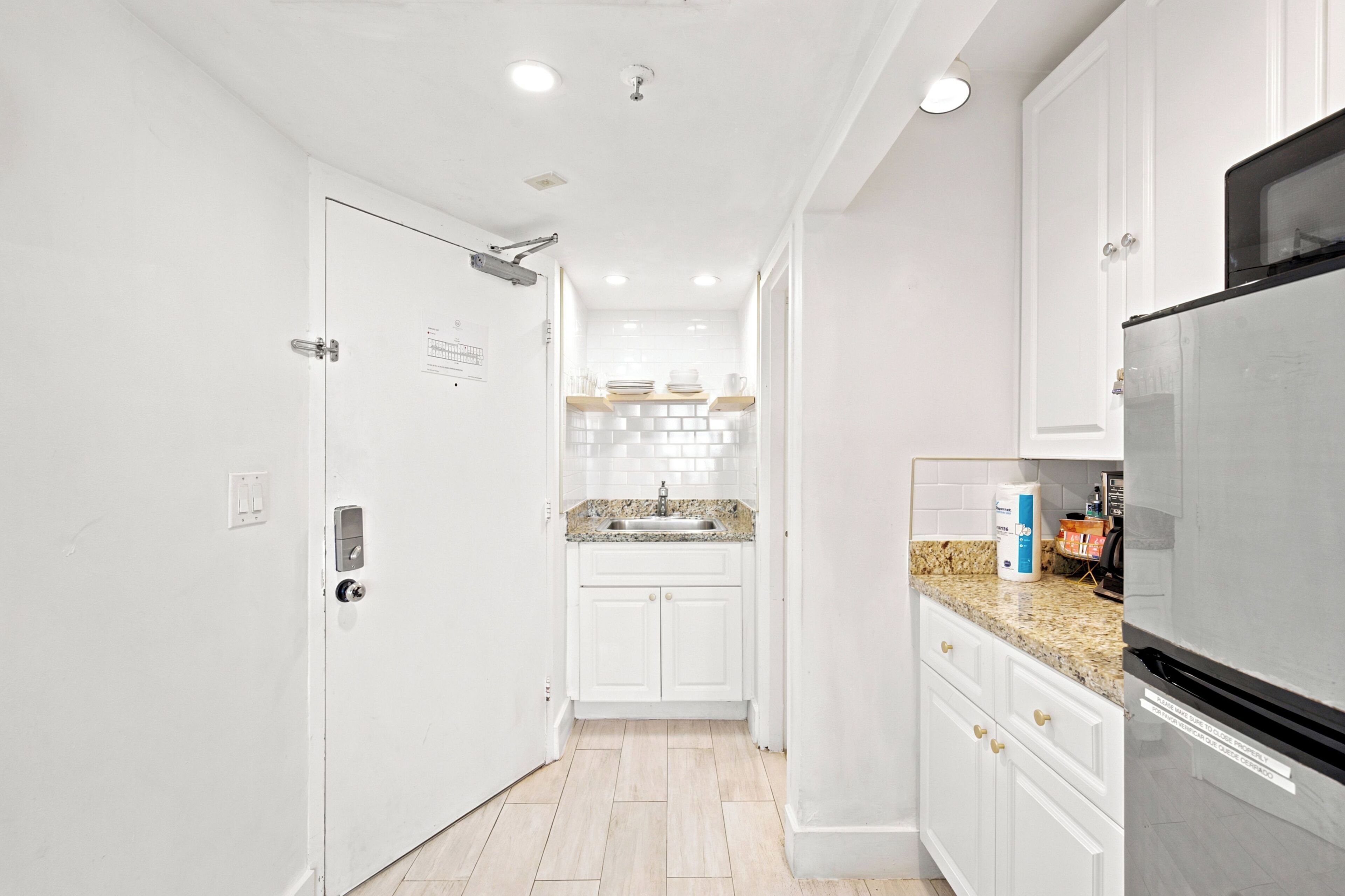 A modern kitchen with white cabinetry, a granite countertop, and a stainless steel refrigerator.