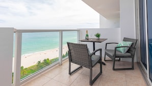 Un balcon avec des fauteuils en osier, une petite table avec une bouteille et un verre, et une vue sur la plage.