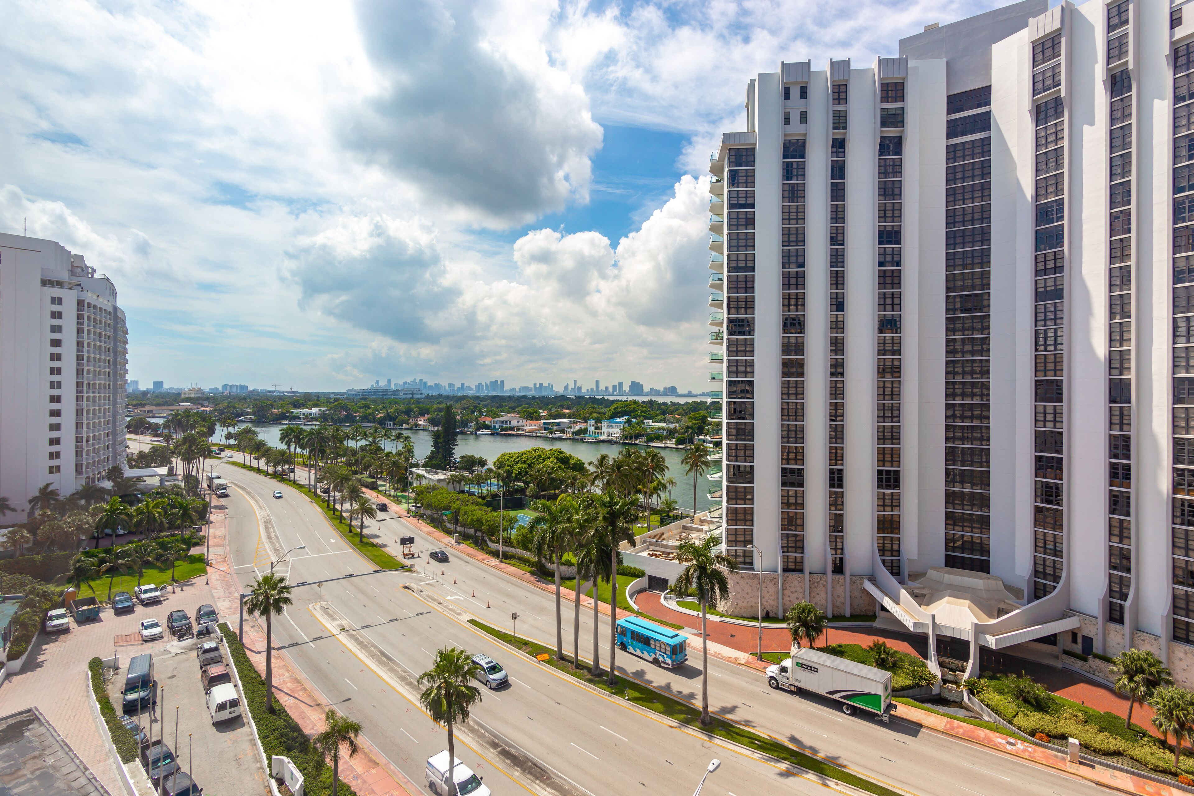 A modern high-rise hotel with a curved entrance, a view of a river, and a city skyline in the background.