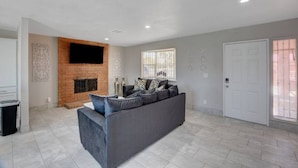A spacious living room with a grey sofa, a fireplace, and a flat-screen TV mounted on the wall.