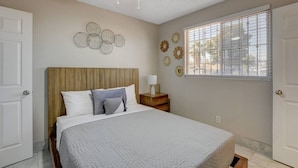 A bedroom with a bed, a ceiling fan, a window with blinds, and decorative wall art.