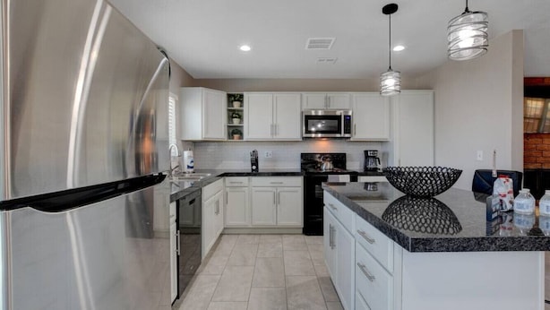 A modern kitchen with stainless steel appliances, white cabinetry, and a granite countertop.