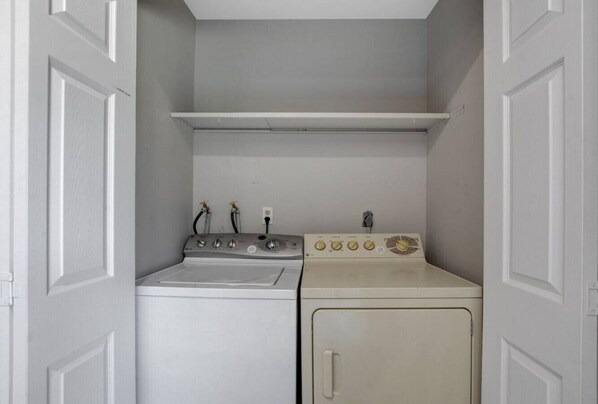A compact laundry room with a washing machine and dryer, a shelf above the dryer, and a door with a handle.