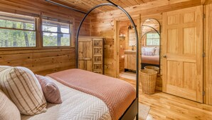 A wooden cabin bedroom with a four-poster bed, a wooden wardrobe, and a large arched doorway leading to a bathroom.