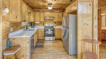 A wooden cabin-style kitchen with a central island, stainless steel appliances, and a ceiling fan.