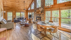 A spacious wooden cabin with a stone fireplace, large windows, and a cozy seating area.