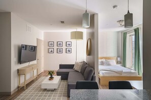 A modern, compact living space with a sofa, a flat-screen TV, a dining table, and a bed with a window view.