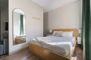 A modern hotel room with a large bed, a bedside table with a lamp, a mirror, and a green curtain.