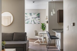 Uma sala de estar moderna com um sofá cinzento, um espelho redondo e uma área de jantar com uma mesa e cadeiras brancas.