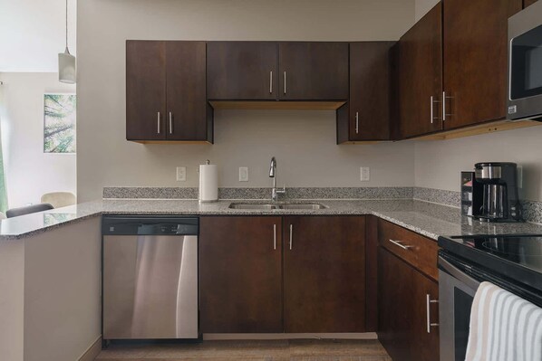 A modern kitchen with dark wood cabinets, a granite countertop, stainless steel appliances, and a coffee maker.
