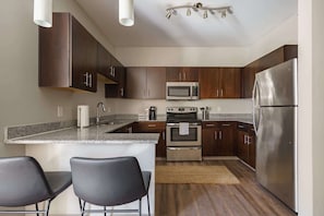 Une cuisine moderne avec des meubles en bois foncé, des appareils électroménagers en acier inoxydable, des comptoirs en granit et des tabourets de bar noirs.
