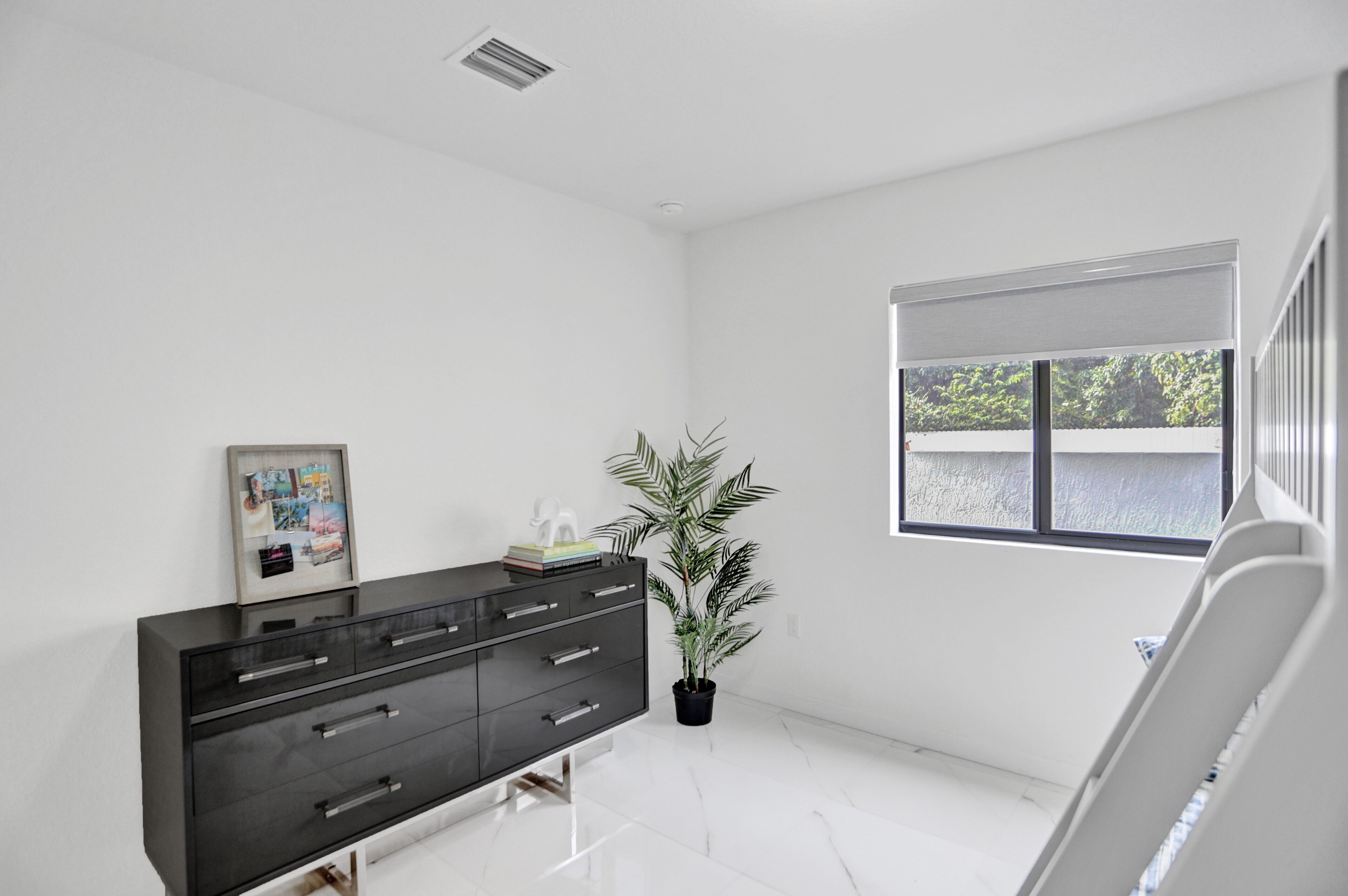 Une chambre moderne et minimaliste, avec une commode noire, une plante en pot et une grande fenêtre.