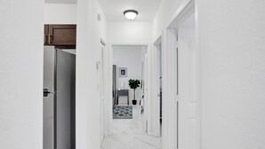 A narrow hallway with white walls and a tiled floor, leading to a room with a door. -  Renzzi Wynwood Apartments (Miami)